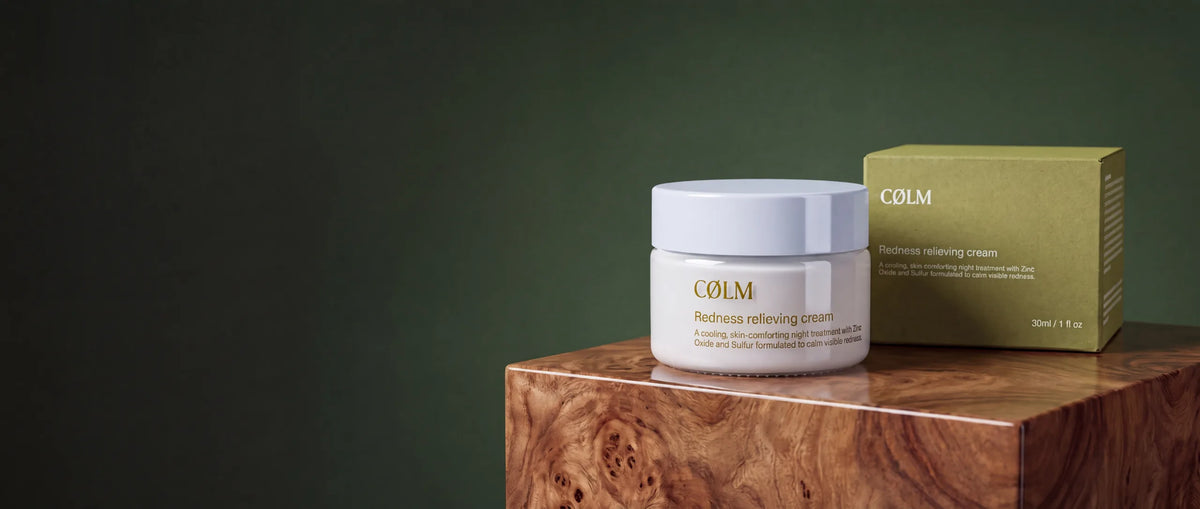 CØLM Redness Relieving Cream — bøtte og æske på træpodie mod mørkegrøn baggrund